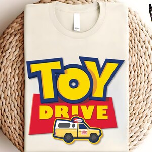 May include: A white t-shirt with a red, yellow, and blue graphic design. The graphic features the words "Toy Drive" and a cartoon image of a yellow toy truck.
