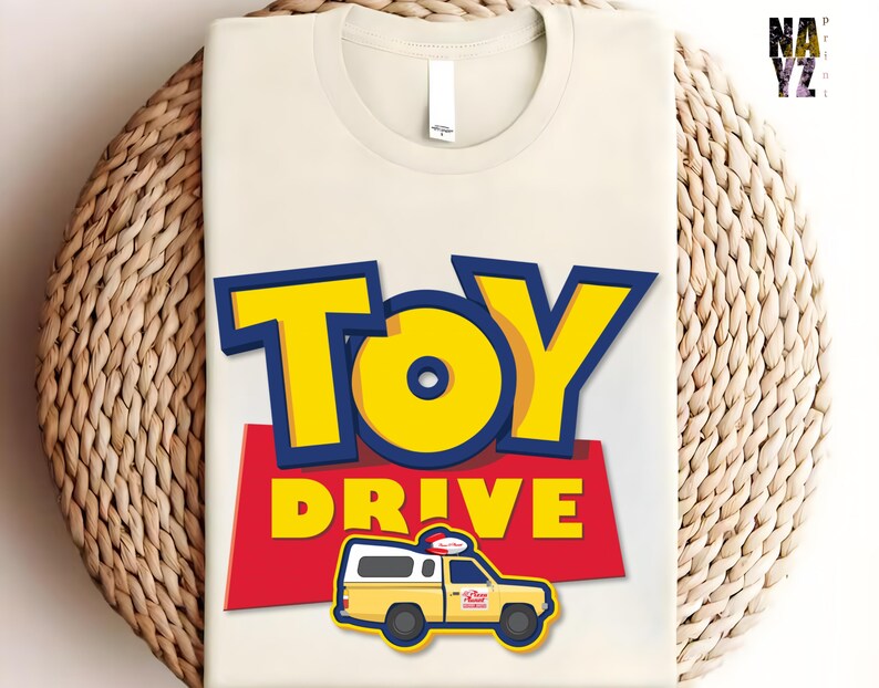 May include: A white t-shirt with a red, yellow, and blue graphic design. The graphic features the words "Toy Drive" and a cartoon image of a yellow toy truck.