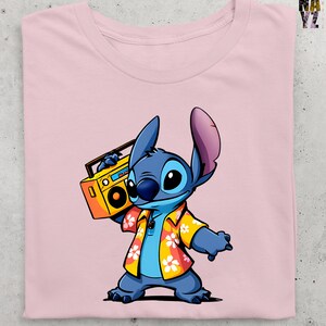 Op de afbeelding: Zachtroze t-shirt met een cartoonillustratie van Stitch uit Lilo & Stitch. Stitch is blauw en draagt een geel Hawaiiaans shirt en houdt een gele boombox vast. Het shirt heeft een effen roze kleur.