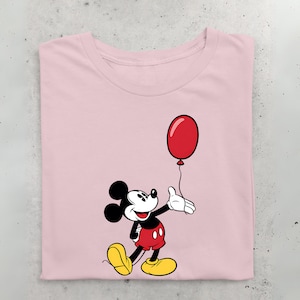 May include: A pink t-shirt with a cartoon image of Mickey Mouse holding a red balloon. Mickey Mouse is wearing his signature red shorts and yellow shoes.