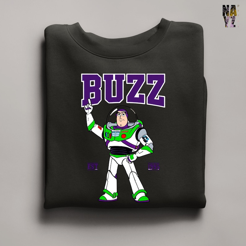 May include: Black sweatshirt featuring a cartoon illustration of Buzz Lightyear in a white and green spacesuit. The word "BUZZ" is printed above the character in purple block letters. The sweatshirt is a crew neck style.
