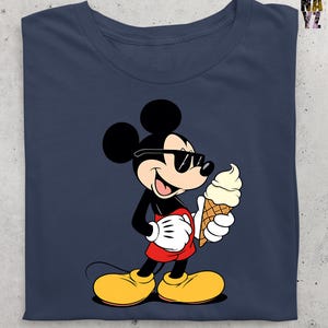 Puede incluir: Camiseta azul marino con un dibujo animado de Mickey Mouse con gafas de sol y un helado. Mickey lleva su atuendo cl&aacute;sico: pantalones cortos rojos, zapatos amarillos y guantes blancos. El cono de helado es de gofre y helado de vainilla.