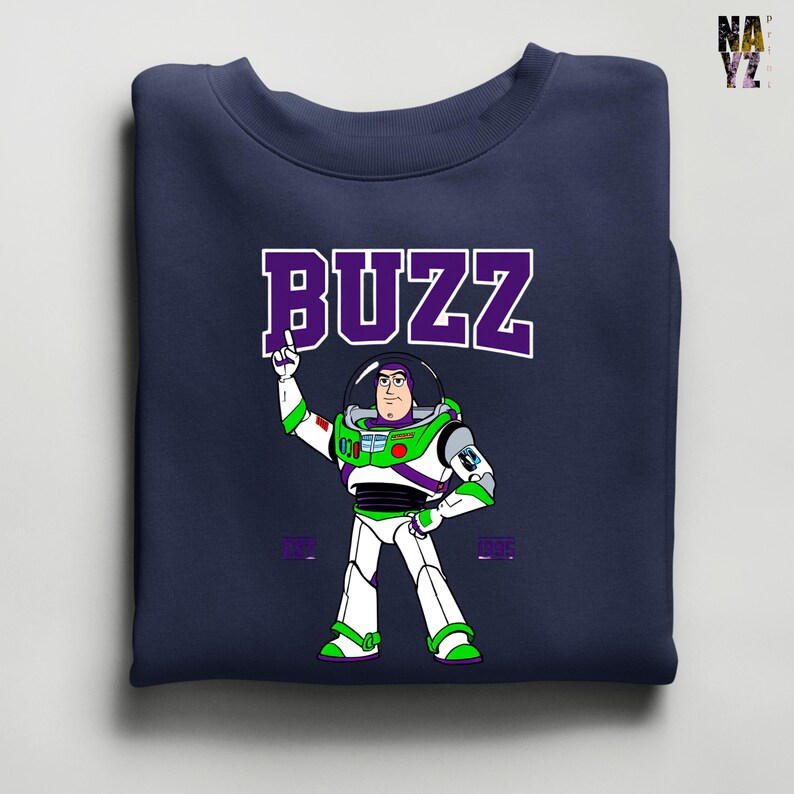 May include: Navy blue sweatshirt featuring a cartoon illustration of Buzz Lightyear from Toy Story. The word "BUZZ" is printed in large, purple letters above the character. Buzz is depicted in his signature white, green, and purple spacesuit, with his arm raised.