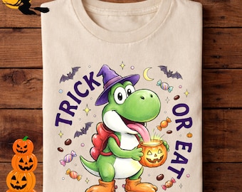 May include: A beige t-shirt featuring a green dinosaur wearing a purple witch hat and holding a jack-o'-lantern bucket. The graphic includes the text "TRICK OR EAT" in purple, surrounded by illustrations of bats, candy, and stars.
