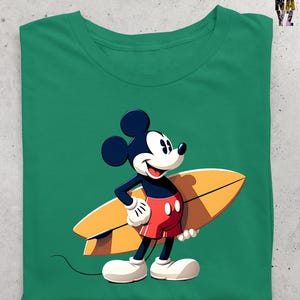 Op de afbeelding: Groen t-shirt met een cartoon illustratie van Mickey Mouse met een surfboard. Mickey draagt een rode broek, witte handschoenen en witte schoenen. Het surfboard is geel en bruin. Een casual kledingstuk.