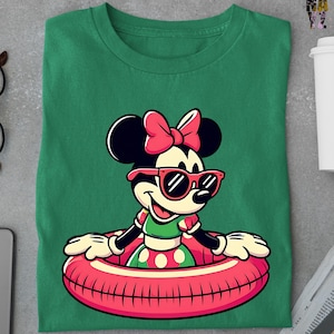 May include: Green t-shirt with a cartoon Minnie Mouse design. Minnie is wearing sunglasses and a pink bow, and is in a red and pink inflatable ring. The design is centered.