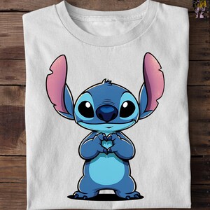 May include: White t-shirt featuring a cartoon character, Stitch, in shades of blue with pink ears. Stitch is making a heart shape with its hands. The shirt is folded on a wooden surface.