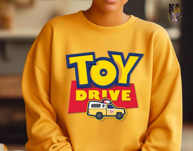 May include: Yellow sweatshirt with a Toy Story themed design. The design features the words "Toy Drive" in a blue and yellow font with a cartoon image of a yellow van with a red roof.
