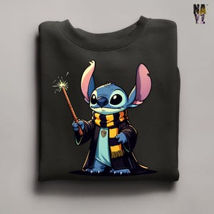 Pode incluir: Camisola preta com um personagem de desenho animado com pele azul, orelhas grandes e um cachecol listrado. O personagem segura uma varinha com um efeito brilhante, vestindo uma t&uacute;nica preta e uma camisa azul clara. O design &eacute; uma mistura l&uacute;dica de fantasia e anima&ccedil;&atilde;o.