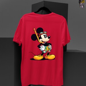 May include: Red t-shirt featuring a cartoon illustration of a mouse wearing a snorkel, goggles, and swim trunks with a duck design. The mouse is standing and smiling, with yellow shoes and a black tail. The shirt is displayed on a black hanger.