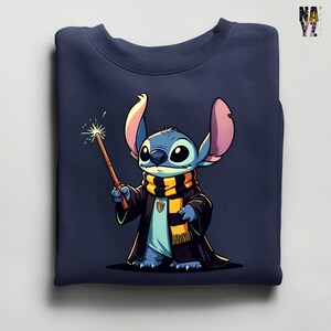Pode incluir: Camisola azul marinho com uma ilustra&ccedil;&atilde;o de desenho animado de Stitch vestido de mago, segurando uma varinha com um efeito brilhante. Stitch est&aacute; usando uma t&uacute;nica preta e um cachecol com listras amarelas e pretas. A camisola est&aacute; dobrada.