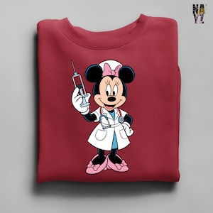 Peut inclure: Sweat-shirt bordeaux avec Minnie Mouse en infirmi&egrave;re, tenant une seringue. Minnie Mouse porte une blouse blanche, un n&oelig;ud rose et un st&eacute;thoscope. Le motif est centr&eacute; sur le devant du sweat-shirt.