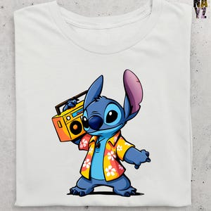 Op de afbeelding: Wit T-shirt met een cartoon illustratie van Stitch die een gele boombox vasthoudt. Stitch is blauw met grote oren en draagt een geel en oranje bloemen shirt. Het ontwerp is gecentreerd op de voorkant van het shirt.