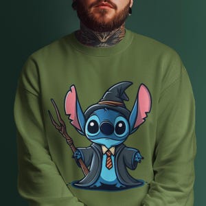 K&ouml;nnte beinhalten: Ein gr&uuml;nes Sweatshirt mit einer blauen Comicfigur, die einen Zaubererhut und eine Robe tr&auml;gt. Die Figur hat gro&szlig;e Augen und ein breites L&auml;cheln. Die Figur h&auml;lt einen Stock mit einem Stern am Ende.