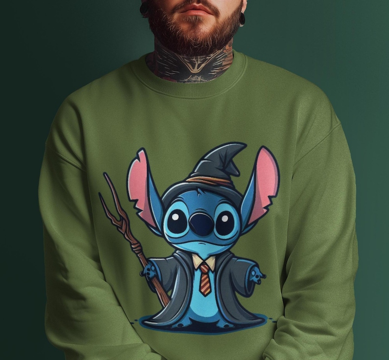 K&ouml;nnte beinhalten: Ein gr&uuml;nes Sweatshirt mit einer blauen Comicfigur, die einen Zaubererhut und eine Robe tr&auml;gt. Die Figur hat gro&szlig;e Augen und ein breites L&auml;cheln. Die Figur h&auml;lt einen Stock mit einem Stern am Ende.