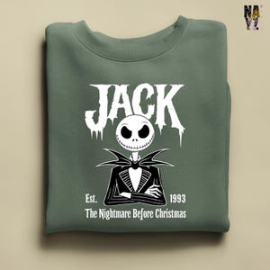 Puede incluir: Sudadera verde salvia con un gr&aacute;fico blanco de Jack Skellington de "Pesadilla antes de Navidad". El dise&ntilde;o incluye la palabra "JACK" en una fuente estilizada sobre una ilustraci&oacute;n de Jack, con el texto "Est. 1993" y "The Nightmare Before Christmas" debajo.