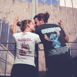 Op de afbeelding: Een stel draagt ​​bijpassende T-shirts met een cartoonfiguurontwerp. Het shirt van de vrouw zegt "Angel" en heeft een roze Stitch-figuur. Het shirt van de man zegt "Stitch" en heeft een blauw Stitch-figuur.