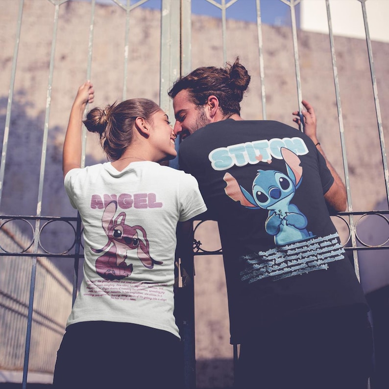 Op de afbeelding: Een stel draagt ​​bijpassende T-shirts met een cartoonfiguurontwerp. Het shirt van de vrouw zegt "Angel" en heeft een roze Stitch-figuur. Het shirt van de man zegt "Stitch" en heeft een blauw Stitch-figuur.