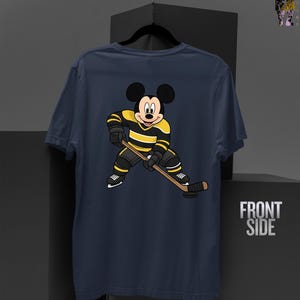 May include: Navy blue t-shirt featuring a cartoon Mickey Mouse in a hockey uniform with black and yellow stripes, holding a hockey stick. The shirt has the words "FRONT SIDE" printed on the right side.