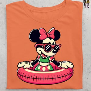 May include: Orange t-shirt with a cartoon Minnie Mouse design. Minnie is wearing sunglasses and a pink bow, and is in a pink and white inflatable ring. She is wearing a green and white polka dot dress. The shirt is folded.