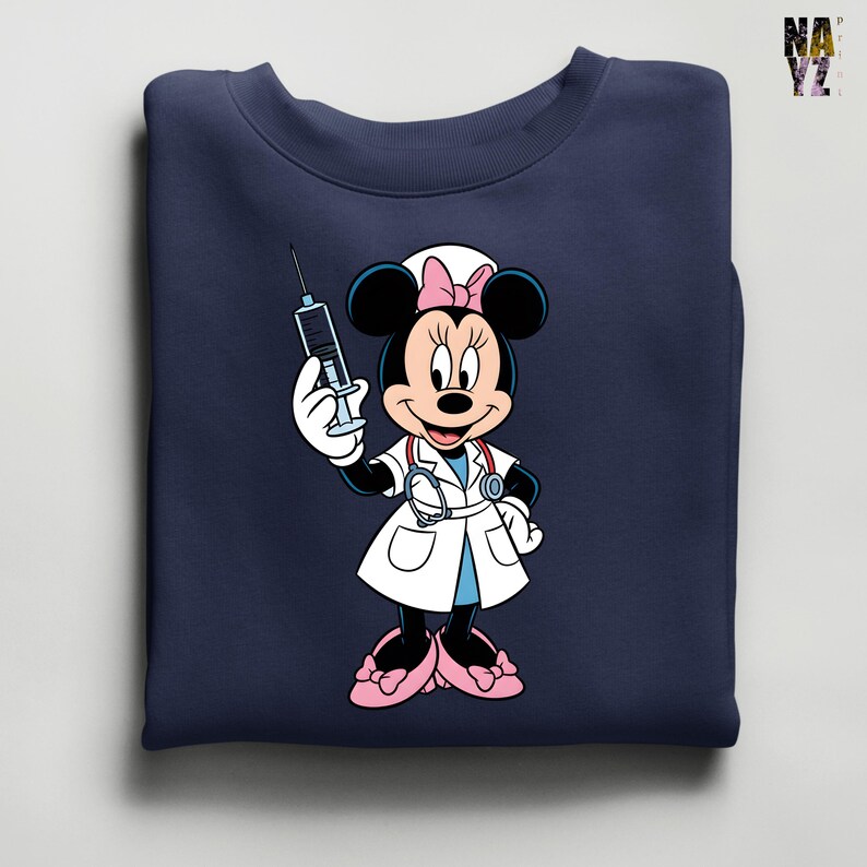 Peut inclure: Sweat-shirt bleu marine avec Minnie Mouse en infirmi&egrave;re tenant une seringue. Minnie porte une blouse blanche, des chaussures roses et un bonnet d'infirmi&egrave;re avec un n&oelig;ud rose. Le sweat-shirt est pli&eacute;.