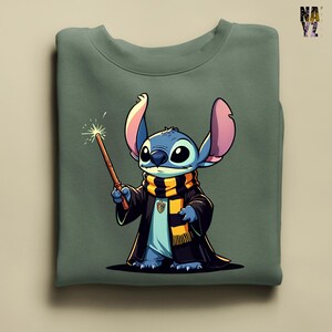 Pode incluir: Camisola verde s&aacute;lvia com uma personagem de desenho animado, azul com orelhas grandes, vestindo uma t&uacute;nica preta e um cachecol amarelo e preto. A personagem segura uma varinha com um efeito brilhante. O design &eacute; uma vers&atilde;o l&uacute;dica do tema do mago.