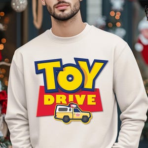 May include: A white sweatshirt with a yellow and blue "Toy Drive" graphic. The graphic features a cartoon toy truck with a pizza delivery logo.