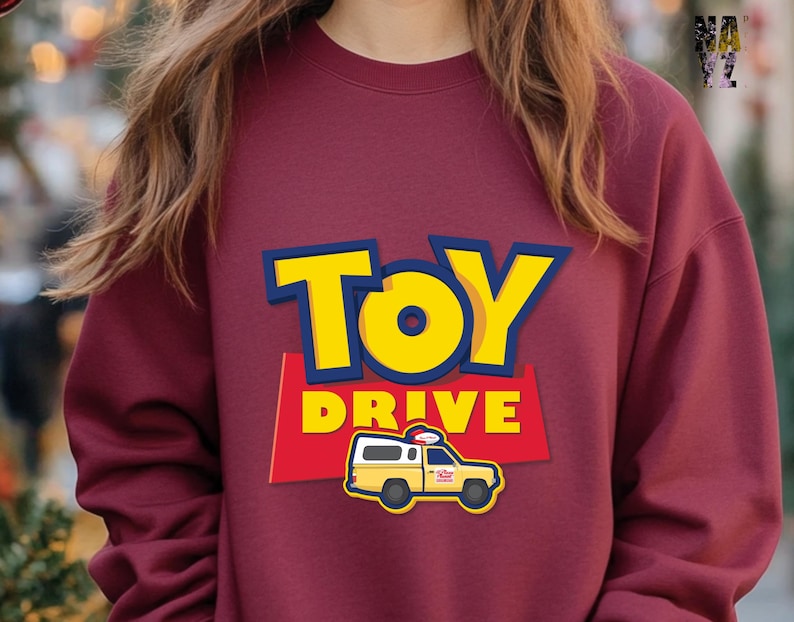 May include: A maroon sweatshirt with a yellow and blue graphic of the words "TOY DRIVE" and a cartoon yellow van with a red roof.