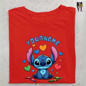 K&ouml;nnte beinhalten: Rotes T-Shirt mit einer blauen Stitch-Figur, umgeben von bunten Herzen und Buntstiften. Der Text "YOURNAME" befindet sich &uuml;ber Stitch.