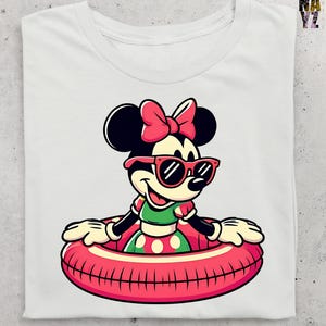May include: White t-shirt with a cartoon Minnie Mouse graphic. Minnie is depicted wearing sunglasses, a pink bow, and a green and red polka dot dress, floating in a red inner tube. The design is centered on the shirt.