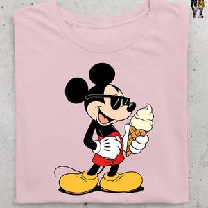 Puede incluir: Camiseta rosa claro con un dibujo de Mickey Mouse con gafas de sol y un helado. Mickey lleva pantalones cortos rojos, zapatos amarillos y guantes blancos. La camiseta tiene el texto "NAVY" y "YZ" en la esquina superior derecha.