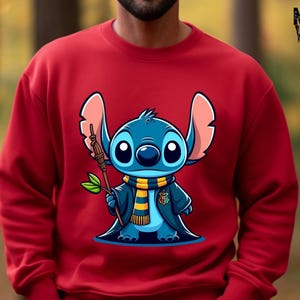 May include: Red sweatshirt with a blue cartoon character wearing a yellow and black scarf and a black robe. The character is holding a stick and has large blue eyes.