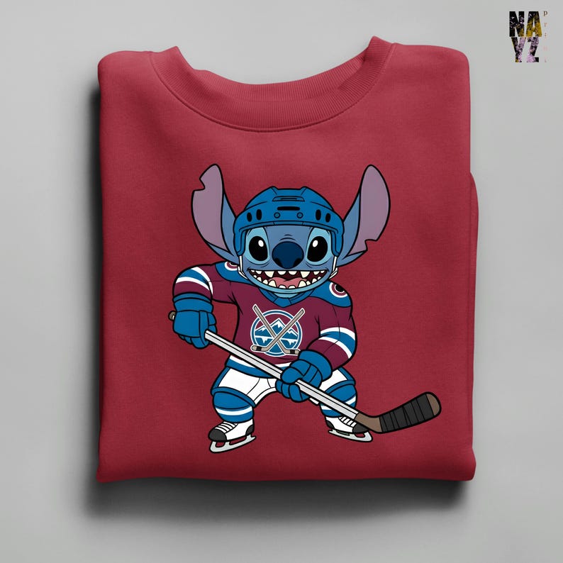 Puede incluir: Una sudadera granate con un personaje de dibujos animados, Stitch, vestido con equipo de hockey. Stitch lleva un casco azul y una camiseta granate y azul con un logotipo de palos de hockey cruzados. Sostiene un palo de hockey y lleva patines.