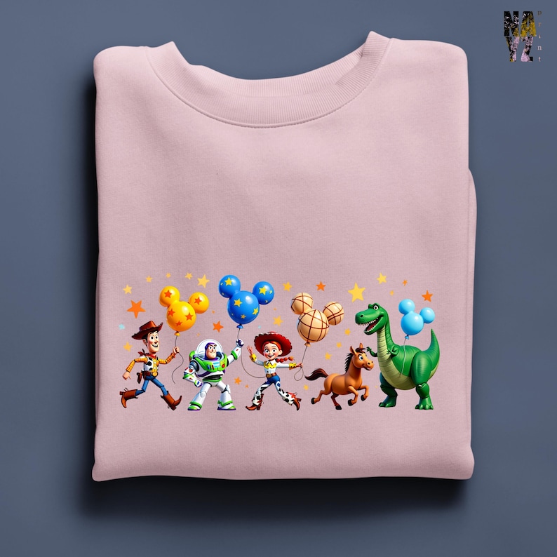 Puede incluir: Sudadera rosa claro con un gr&aacute;fico colorido de personajes de Toy Story. Los personajes sostienen globos con forma de Mickey Mouse sobre un fondo de estrellas.