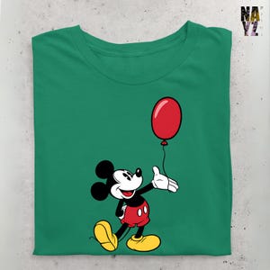 May include: A green t-shirt with a cartoon image of Mickey Mouse holding a red balloon. Mickey Mouse is wearing red shorts with black buttons and yellow shoes.