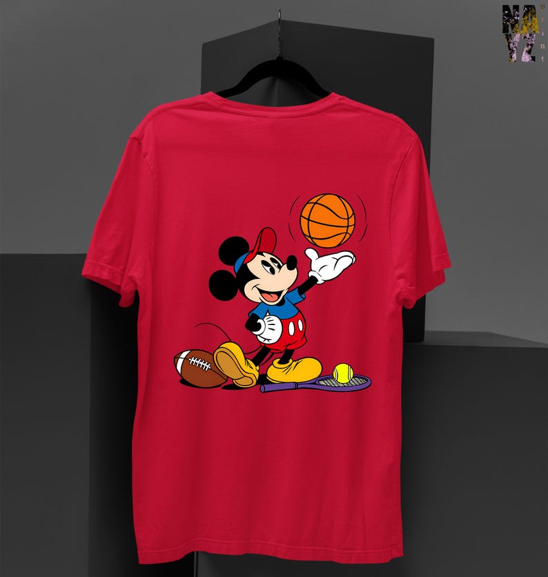 May include: Red t-shirt featuring a cartoon Mickey Mouse character. Mickey is depicted in a blue shirt, red shorts, and yellow shoes, holding a basketball. A football and tennis racket are also present.