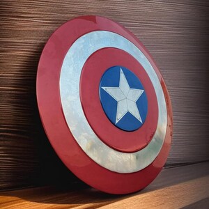 May include: A Captain America shield, featuring a red outer ring, a silver inner ring, and a blue center with a white star. The shield is leaning against a wooden surface, with light and shadow creating a dramatic effect.