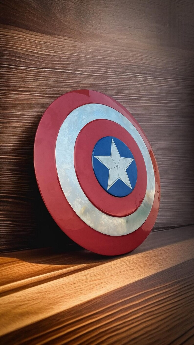 May include: A Captain America shield, featuring a red outer ring, a silver inner ring, and a blue center with a white star. The shield is leaning against a wooden surface, with light and shadow creating a dramatic effect.