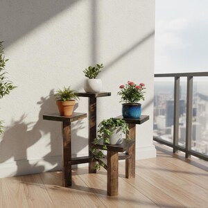 Puede incluir: Un estante de madera marr&oacute;n oscuro de varios niveles con cuatro plantas en macetas. Las plantas incluyen un helecho en una maceta de terracota, una suculenta en una maceta blanca, una planta con flores en una maceta azul y una planta colgante en una maceta gris.