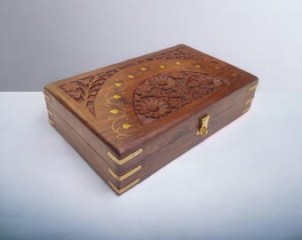 May include: A wooden box with intricate carvings and brass accents. The lid features a floral design with a half-circle pattern.