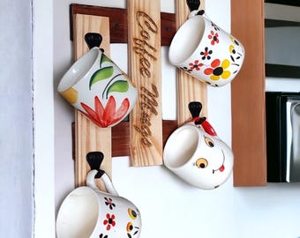 May include: A wooden coffee mug rack with four decorative mugs. The mugs have floral and whimsical designs. The rack has the words "Coffee Mugs" etched into the wood.