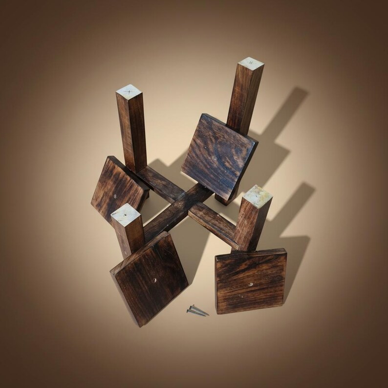 Puede incluir: Un soporte de madera para plantas con un dise&ntilde;o geom&eacute;trico. El soporte est&aacute; hecho de madera marr&oacute;n oscuro con una base cuadrada y cuatro soportes verticales. La parte superior de cada soporte es de un color m&aacute;s claro. Se ven dos tornillos.