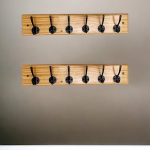 Könnte beinhalten: Zwei Holz-Kleiderständer mit schwarzen Metallhaken. Jeder Ständer hat sieben Haken.