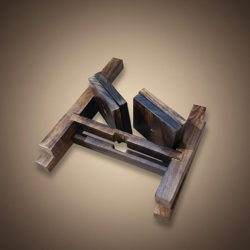 Puede incluir: Un soporte de madera marr&oacute;n oscuro con un dise&ntilde;o geom&eacute;trico. El soporte est&aacute; hecho de piezas de madera entrelazadas, creando una estructura robusta y decorativa. La veta de la madera es visible, lo que a&ntilde;ade a su est&eacute;tica natural.