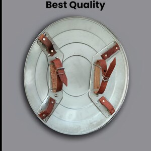 May include: A silver-colored shield with brown leather straps. The shield has a circular design with a central indentation. The text "Leather strip Best Quality" is displayed on the image.