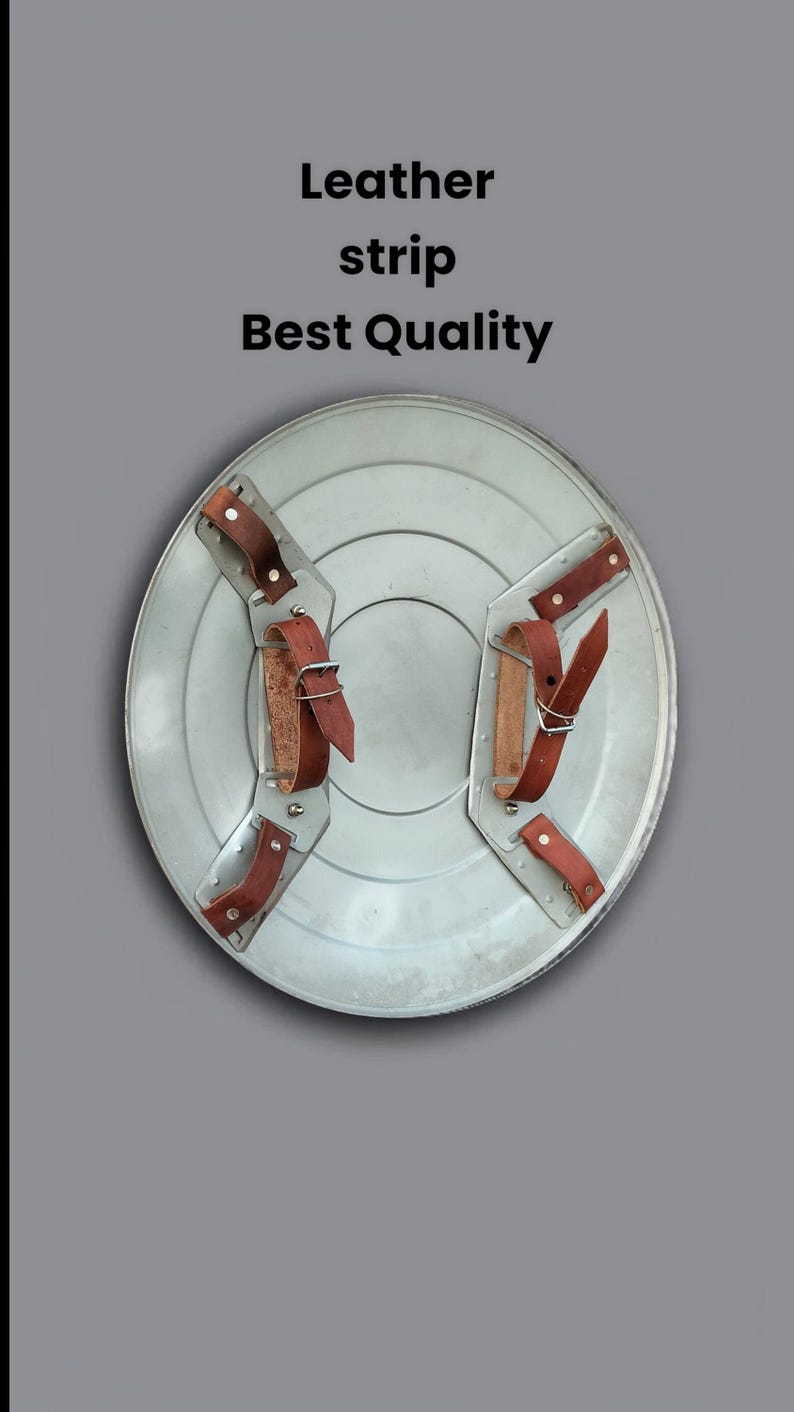 May include: A silver-colored shield with brown leather straps. The shield has a circular design with a central indentation. The text "Leather strip Best Quality" is displayed on the image.