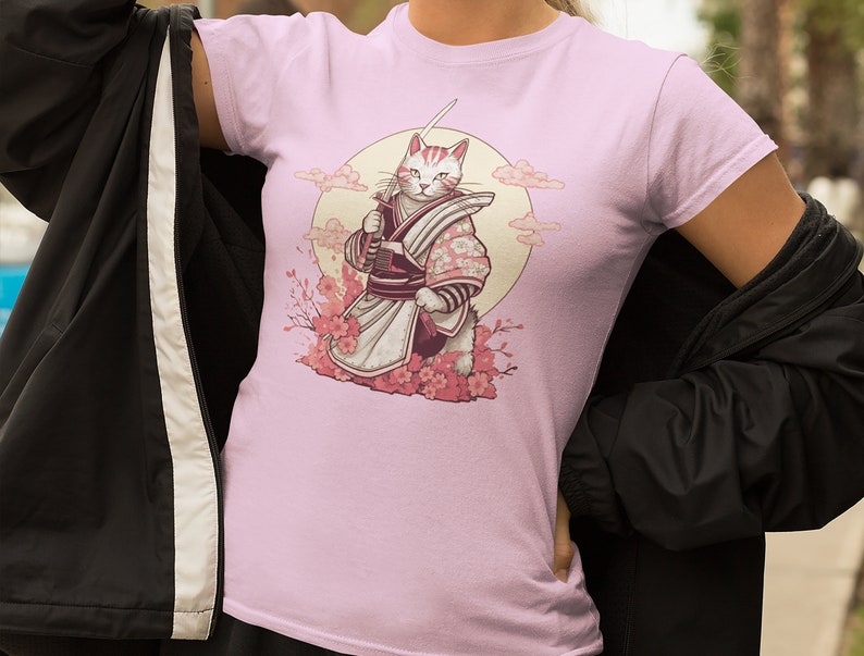 K&ouml;nnte beinhalten: Pinkes T-Shirt mit einem Grafikdruck eines wei&szlig;en Katers, der als Samurai verkleidet ist und ein Schwert vor einem Vollmond und Kirschbl&uuml;ten h&auml;lt.