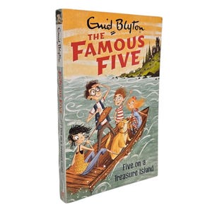 May include: A hardcover book titled "The Famous Five" by Enid Blyton. The cover illustration depicts five children and a dog in a wooden boat on water, with a castle in the background. The book is titled "Five on a Treasure Island".