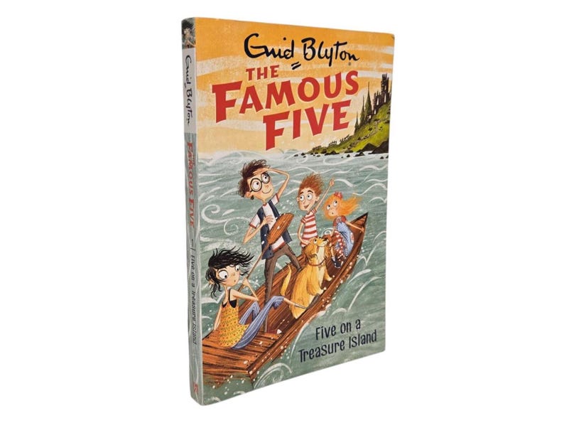 May include: A hardcover book titled "The Famous Five" by Enid Blyton. The cover illustration depicts five children and a dog in a wooden boat on water, with a castle in the background. The book is titled "Five on a Treasure Island".
