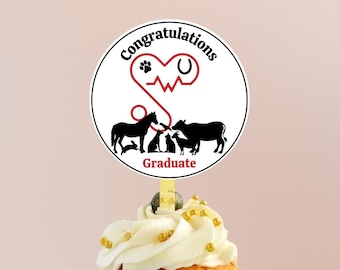 May include: A white cupcake with white frosting and gold sprinkles topped with a round, white sticker that says "Congratulations" with a red heart, a horseshoe, a paw print, and a red EKG line. The sticker also has black silhouettes of a horse, a cat, a goat, a dog, and a cow. The sticker also says "Graduate" at the bottom.